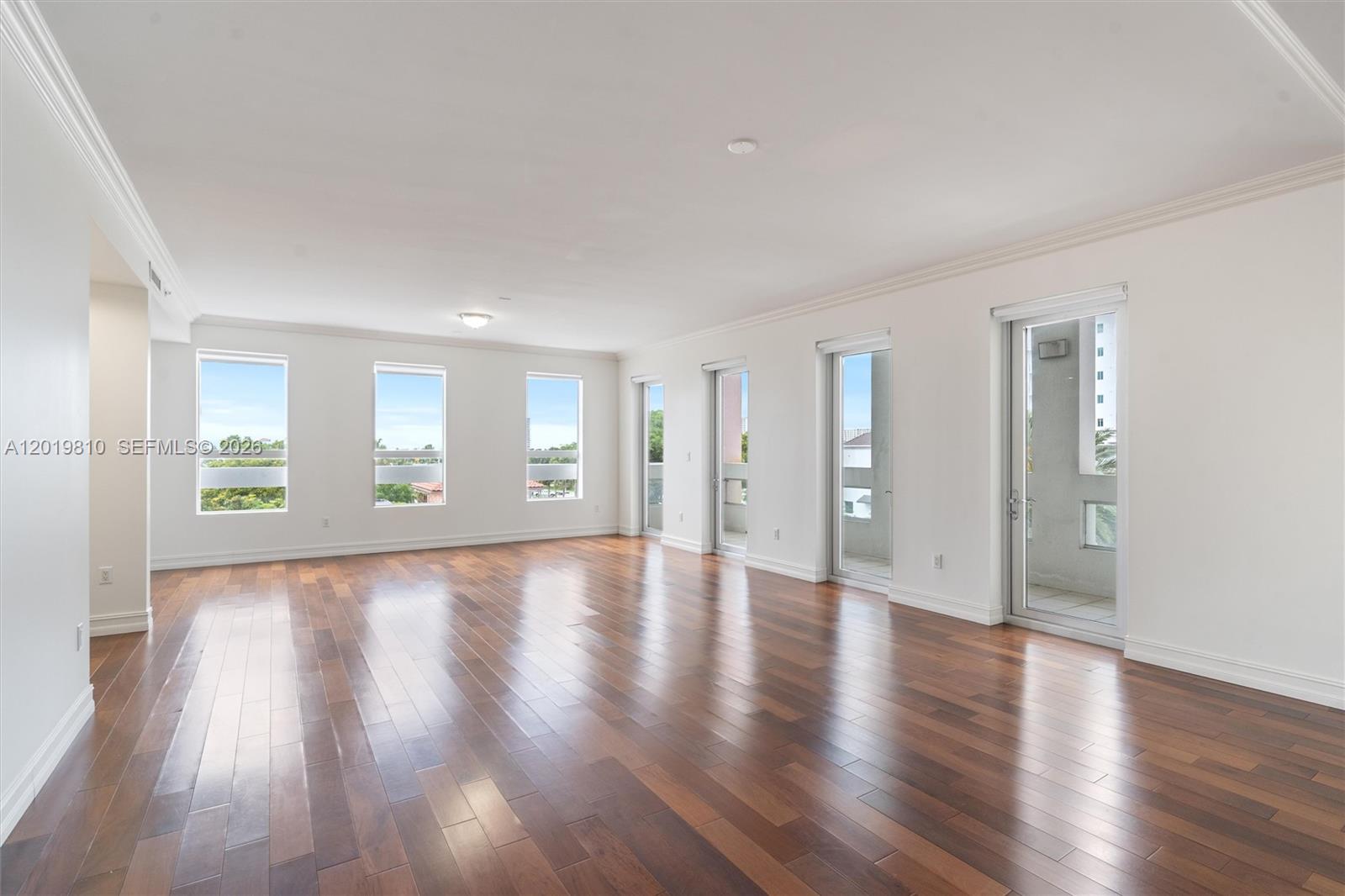 An empty room features dark wood flooring, white walls, and multiple windows and glass doors — 455 E Palmetto Park Rd # 4E, Boca Raton FL 33432, BOCA RATON, FL