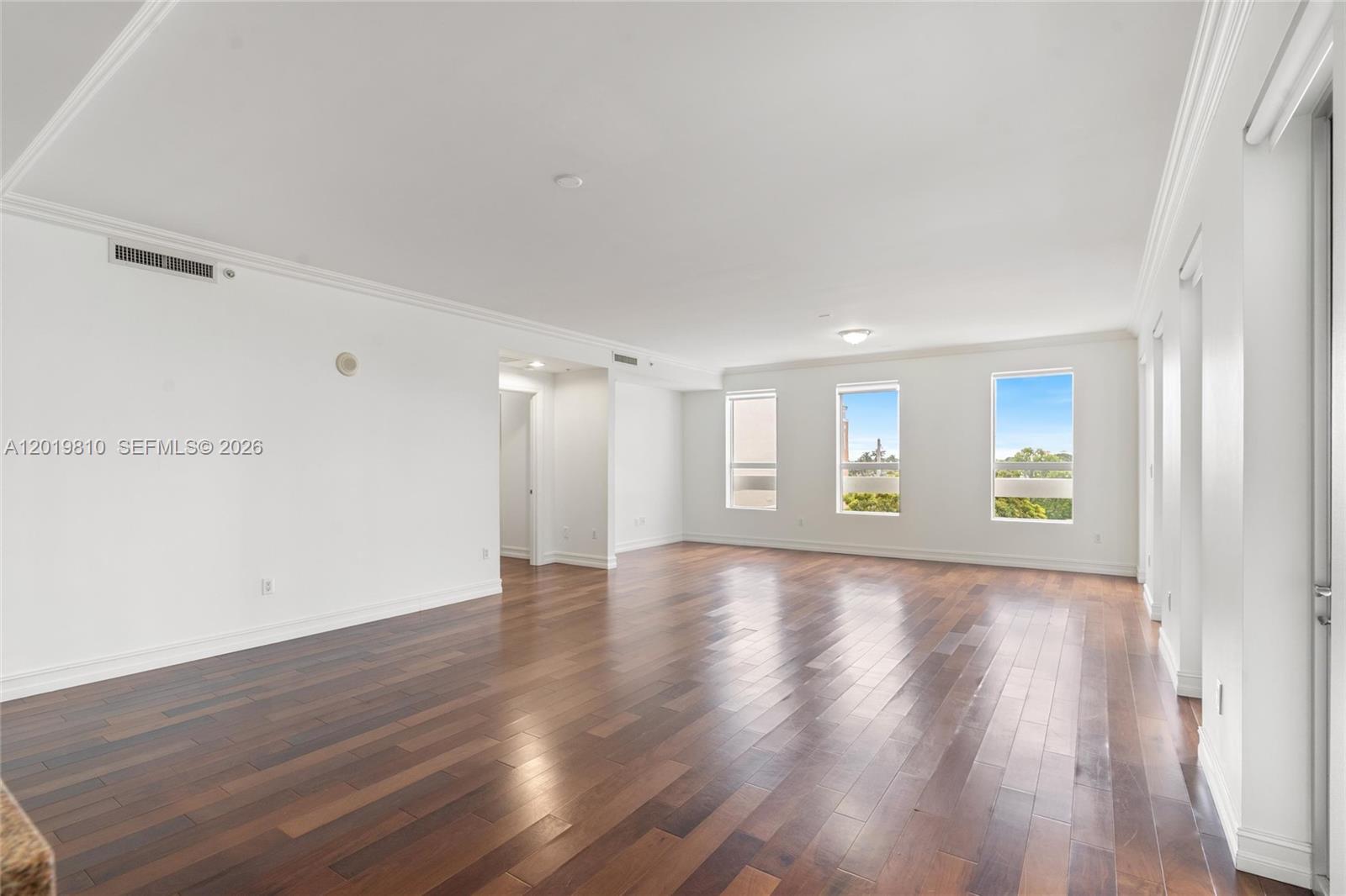 An empty living room features dark hardwood floors, white walls, and three large windows — 455 E Palmetto Park Rd # 4E, Boca Raton FL 33432, BOCA RATON, FL