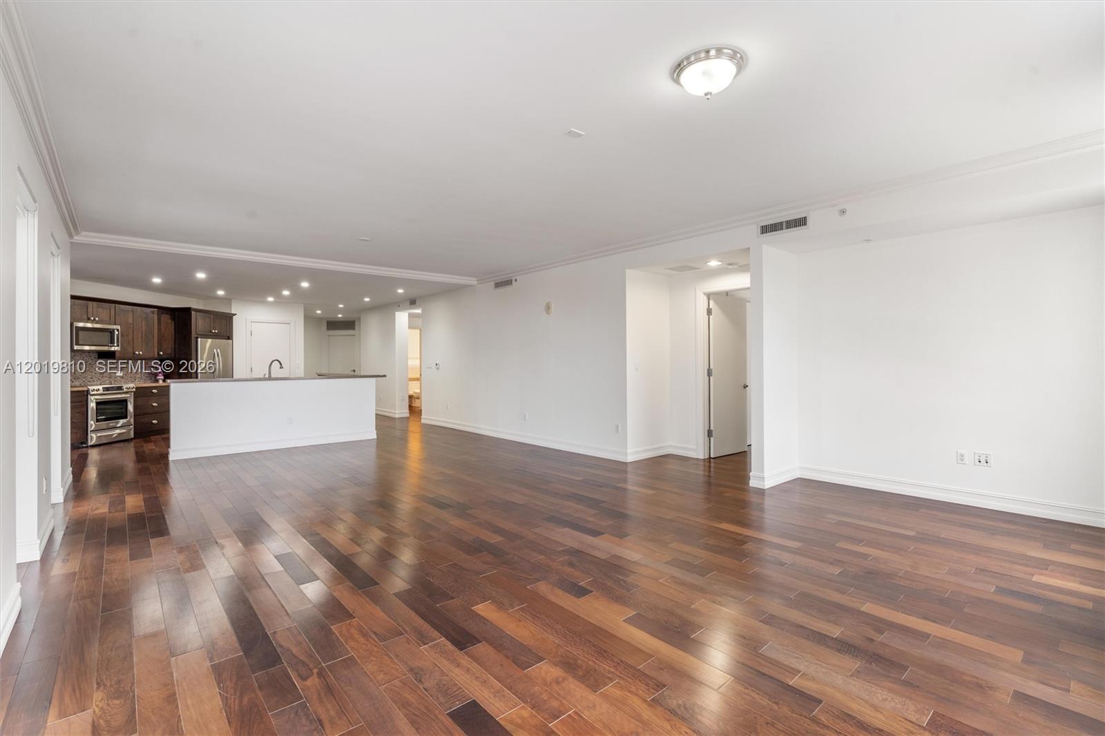 An open-concept living area features dark hardwood floors, white walls, and an adjacent kitchen — 455 E Palmetto Park Rd # 4E, Boca Raton FL 33432, BOCA RATON, FL