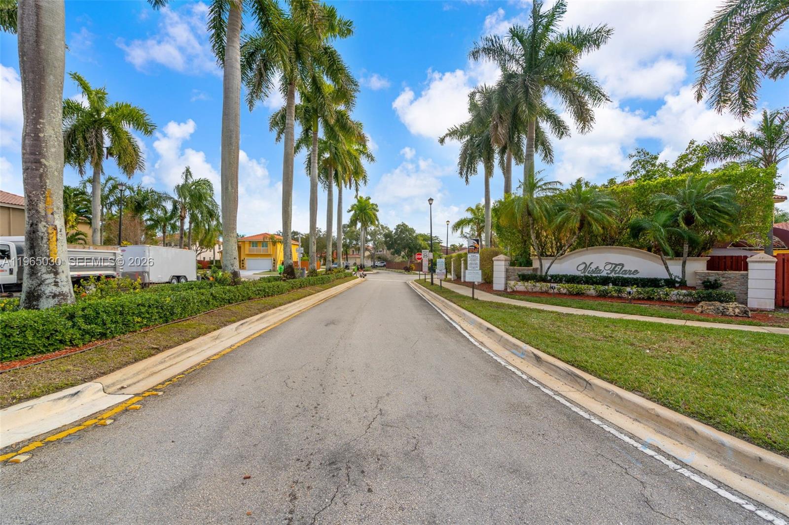 A paved road leads into a residential community entrance with palm trees and signage — 14734 Via Tivoli Ct, Davie FL 33325, DAVIE, FL