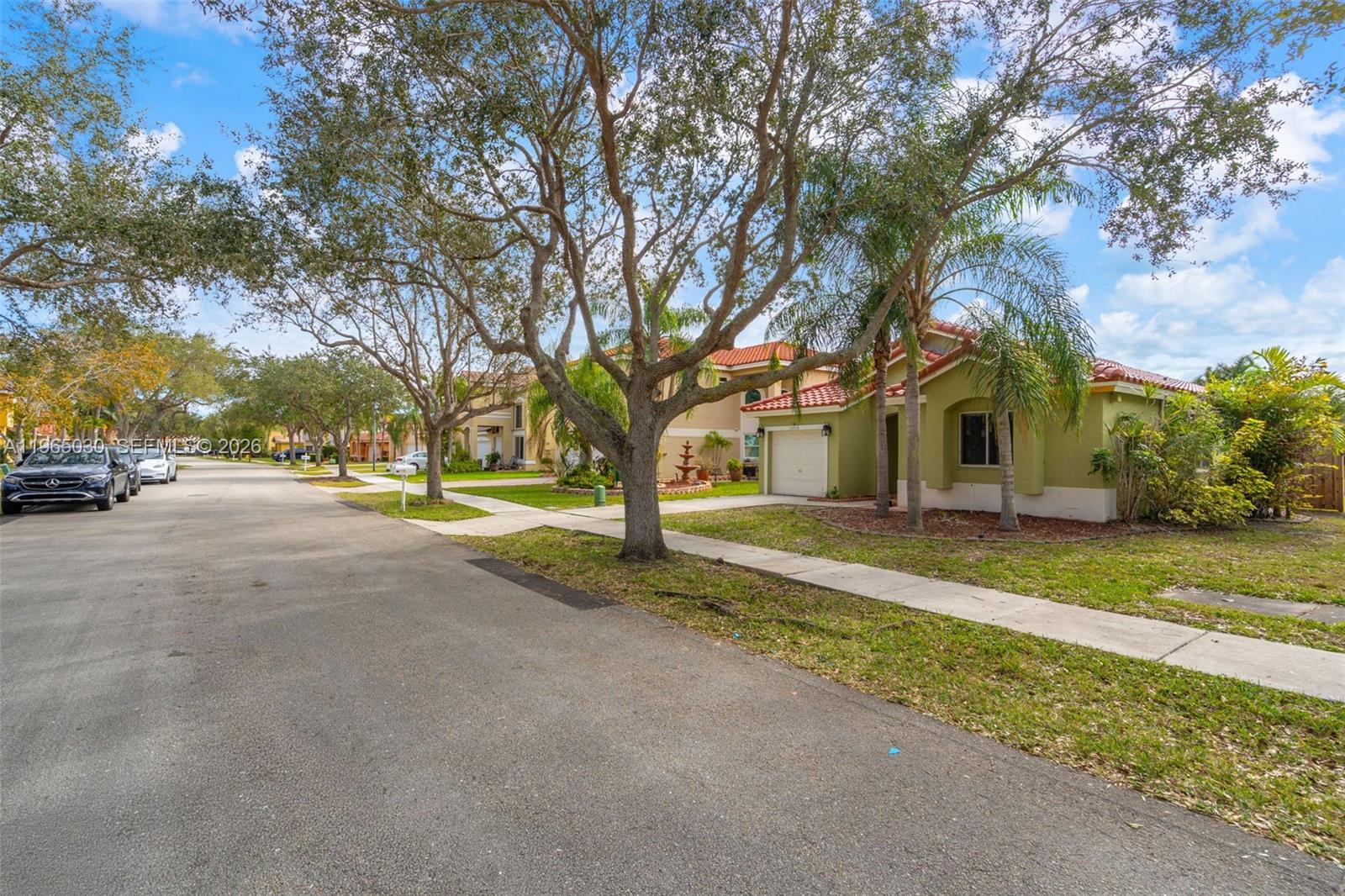 A street view of a suburban neighborhood featuring a green house with a tiled roof — 14734 Via Tivoli Ct, Davie FL 33325, DAVIE, FL