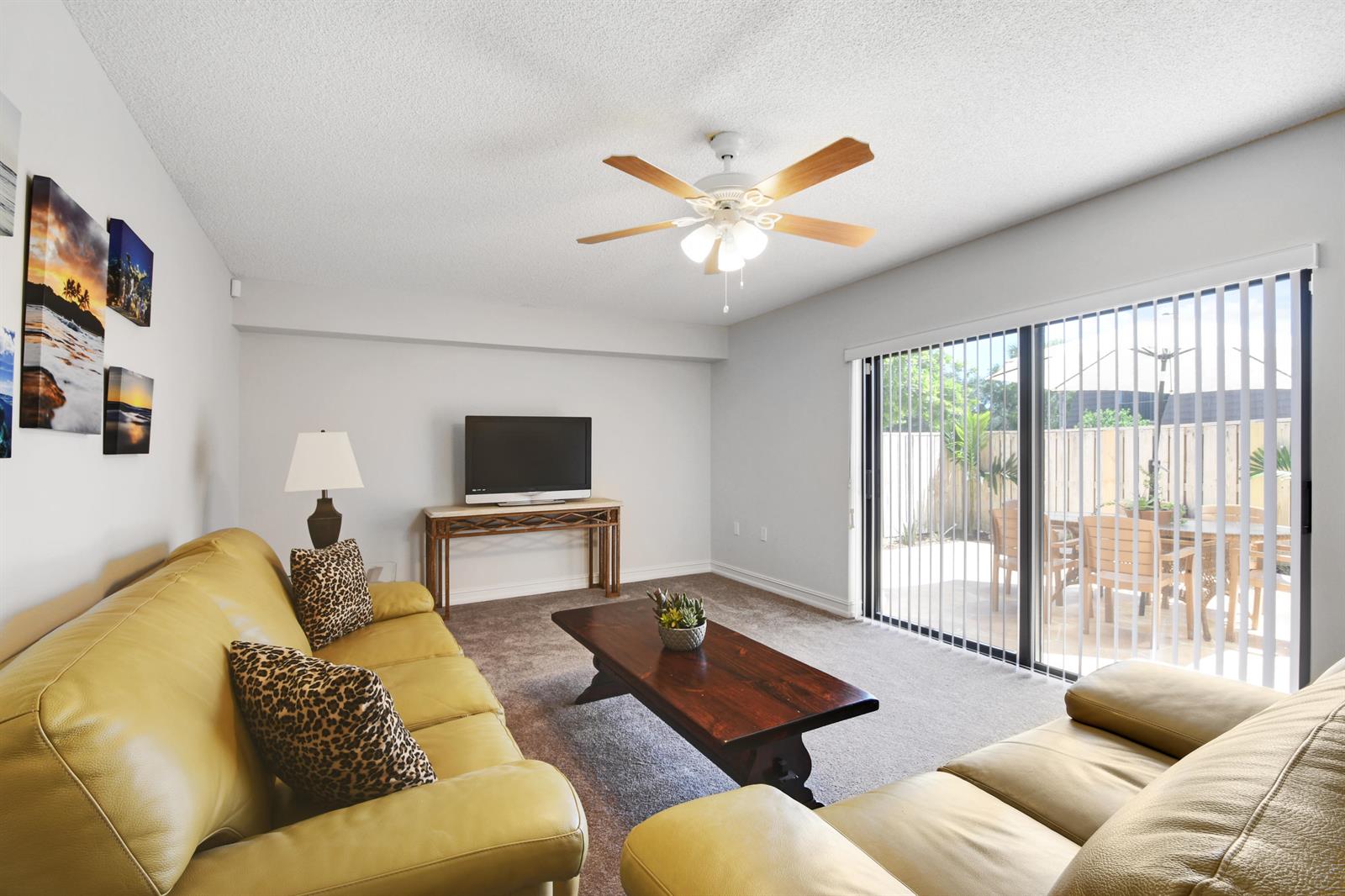 A living room features a yellow leather sofa, a dark wood coffee table, and sliding doors — 1603 16th Court, Jupiter FL 33477, JUPITER, FL
