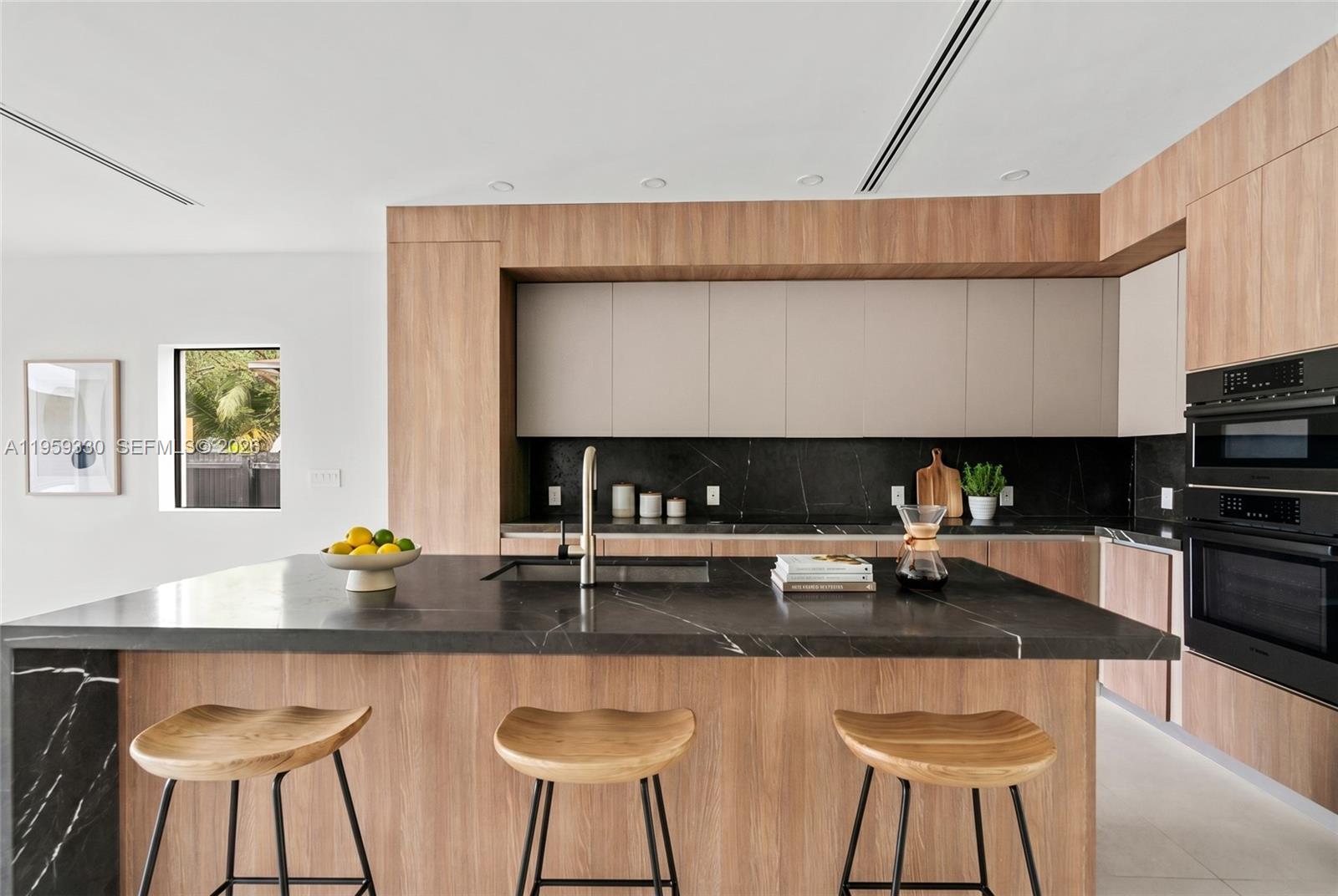 A modern kitchen features a black marble island, wood cabinetry, and built-in wall ovens — 1431 SW 20th St, Miami FL 33145, MIAMI, FL