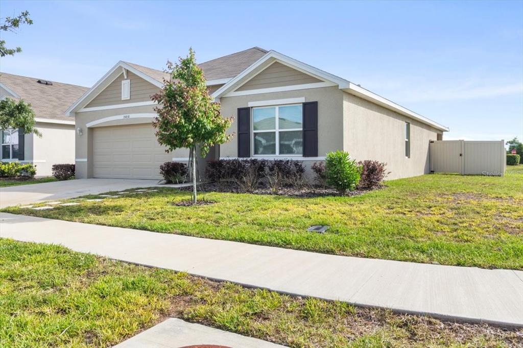 A single-story suburban house with a tan stucco exterior, a two-car garage, and a lawn — 35830 ELLSWORTH PLACE, ZEPHYRHILLS, FL