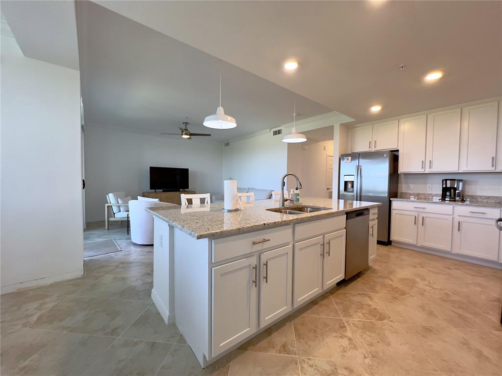A kitchen with white cabinets, granite countertops, and an island overlooks a living area — 14051 HERITAGE LANDING BOULEVARD UNIT 537, PUNTA GORDA, FL