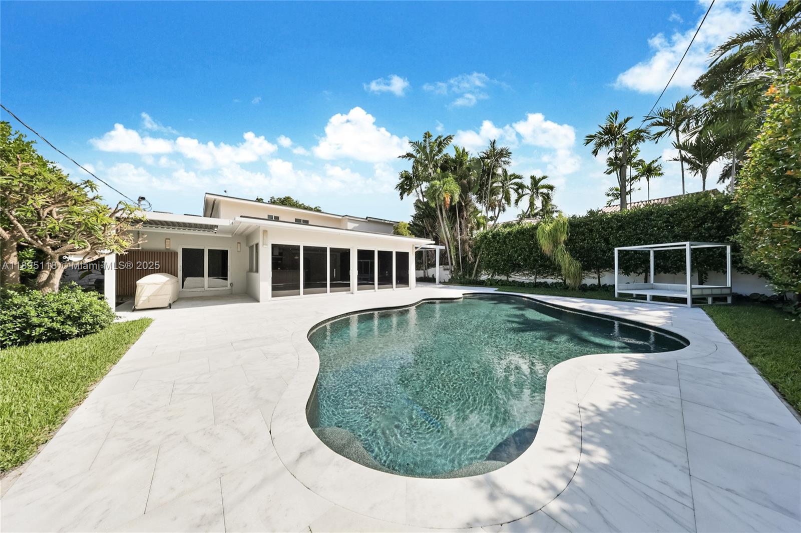 A backyard features a kidney-shaped swimming pool surrounded by white stone pavers and landscaping — 5244 Alton Rd, Miami Beach FL 33140, MIAMI BEACH, FL