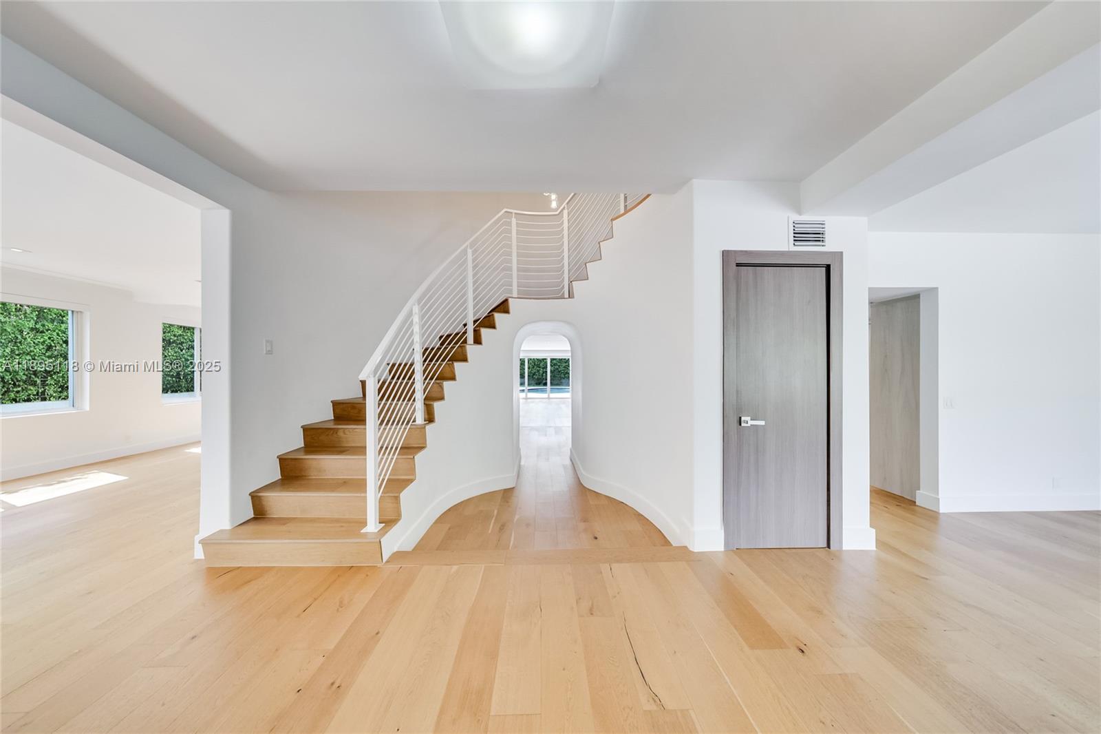 A modern interior features a light wood staircase with white railings and a curved entryway — 5244 Alton Rd, Miami Beach FL 33140, MIAMI BEACH, FL