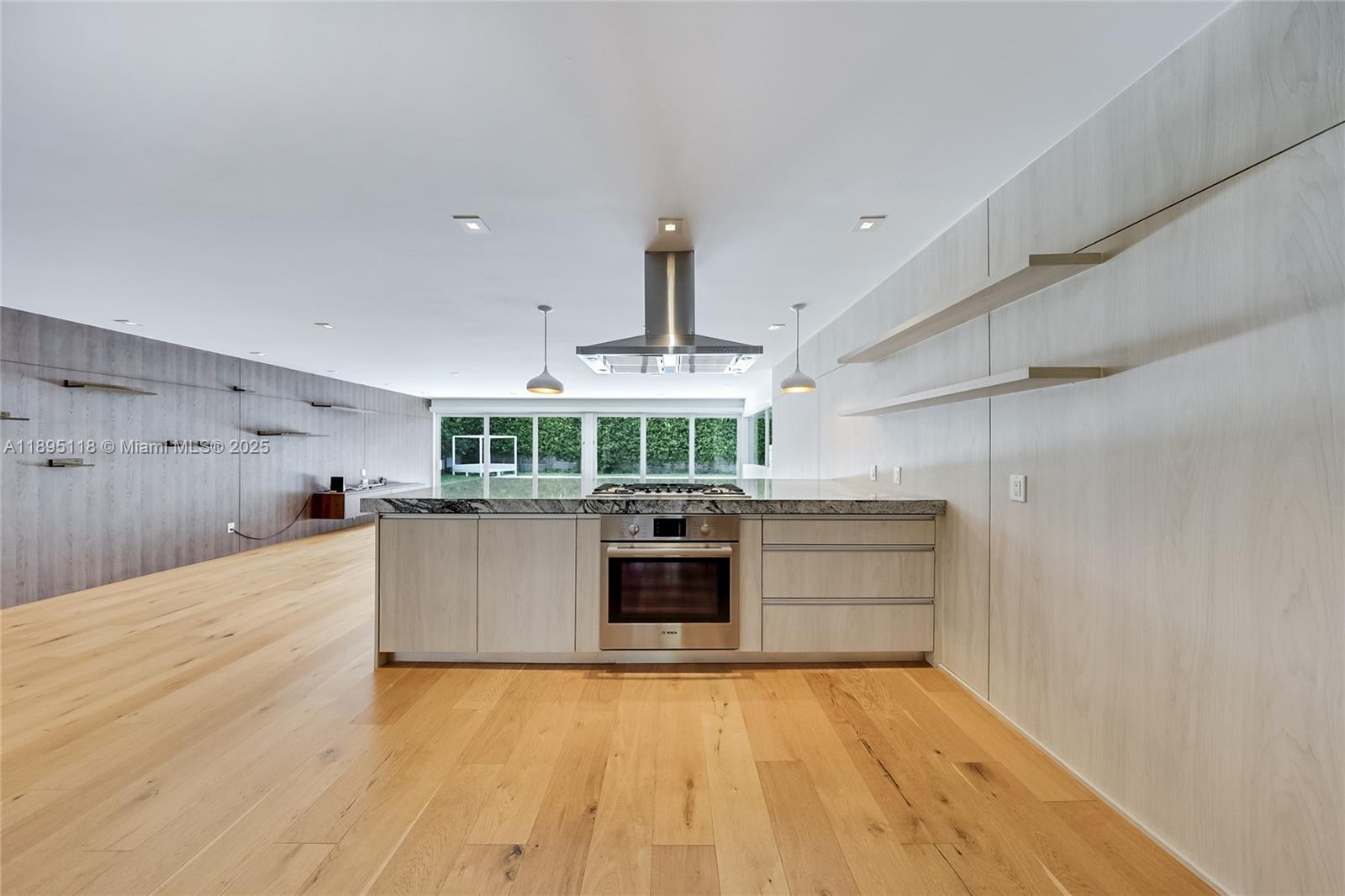 A modern kitchen features a central island with a built-in oven and light wood cabinetry — 5244 Alton Rd, Miami Beach FL 33140, MIAMI BEACH, FL