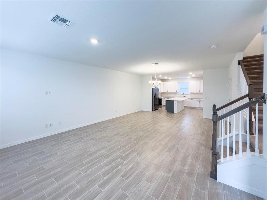 An open-concept living area features light wood-look tile flooring and a kitchen with white cabinets — 6483 TRAILBLAZE BEND, ST CLOUD, FL
