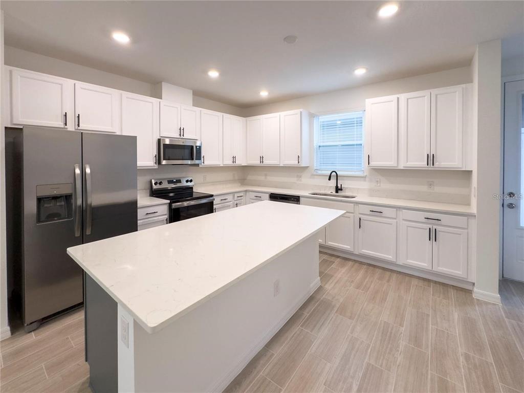 A modern kitchen features white cabinets, stainless steel appliances, a large island, and light flooring — 6483 TRAILBLAZE BEND, ST CLOUD, FL