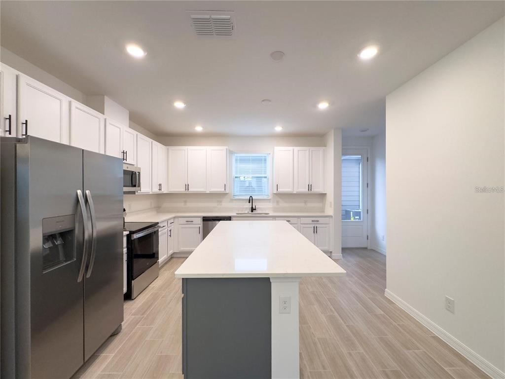 A modern kitchen features white cabinets, stainless steel appliances, a gray island, and light flooring — 6483 TRAILBLAZE BEND, ST CLOUD, FL