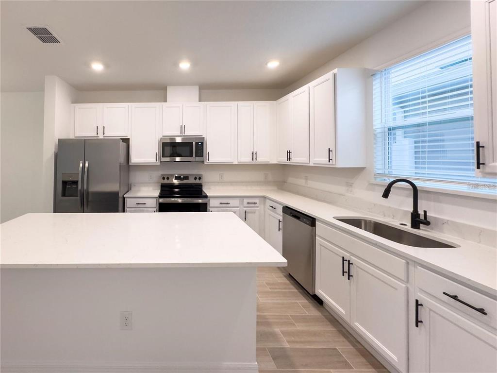 A modern kitchen features white cabinets, stainless steel appliances, and a large white quartz island — 6483 TRAILBLAZE BEND, ST CLOUD, FL