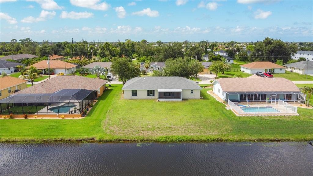 An aerial view of three suburban houses along a canal, featuring pools and screened lanais — 104 MARK TWAIN LANE, ROTONDA WEST, FL