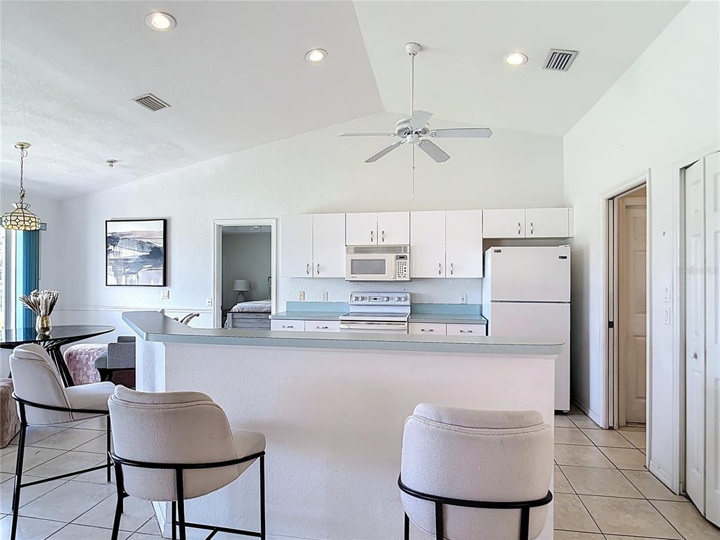 A kitchen with white cabinets, a breakfast bar, and stools overlooks a dining area — 104 MARK TWAIN LANE, ROTONDA WEST, FL