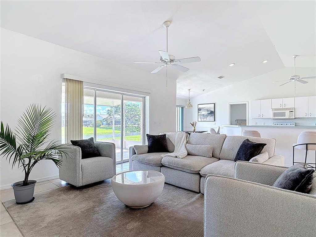 A living room with a sectional sofa, armchairs, and a sliding door overlooking a pond — 104 MARK TWAIN LANE, ROTONDA WEST, FL