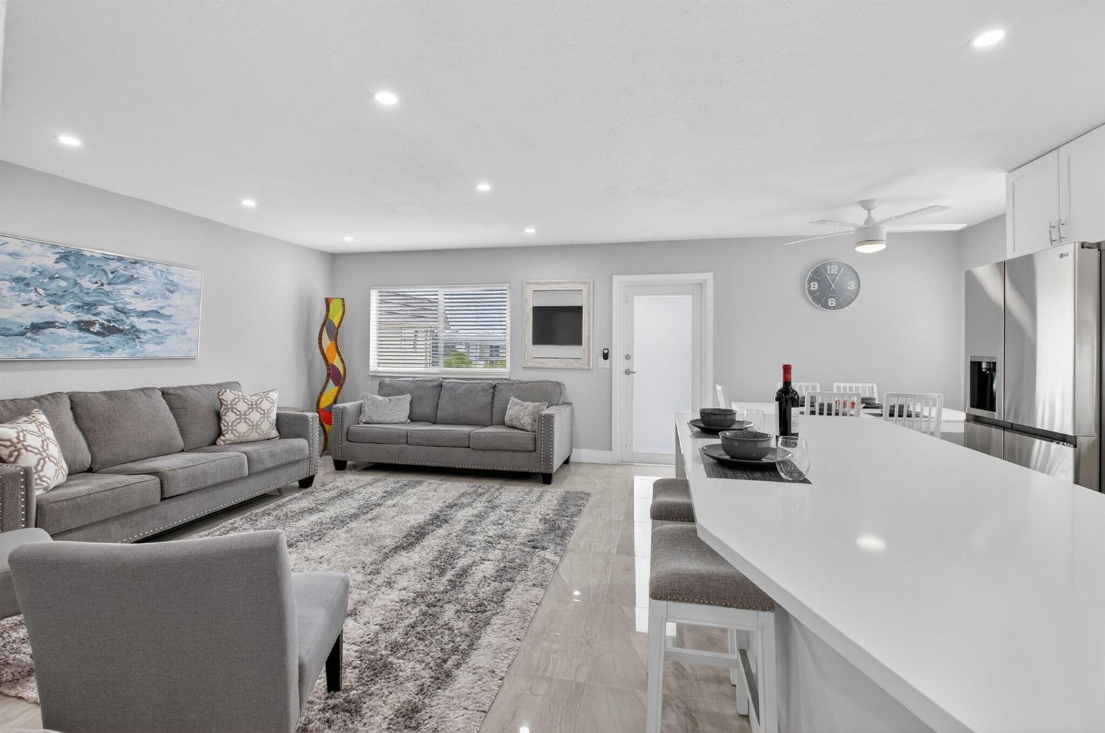 A modern open-concept living room and kitchen featuring gray sofas, a white island, and tile flooring — 321 Saxony Trail # G, Delray Beach FL 33446, DELRAY BEACH, FL