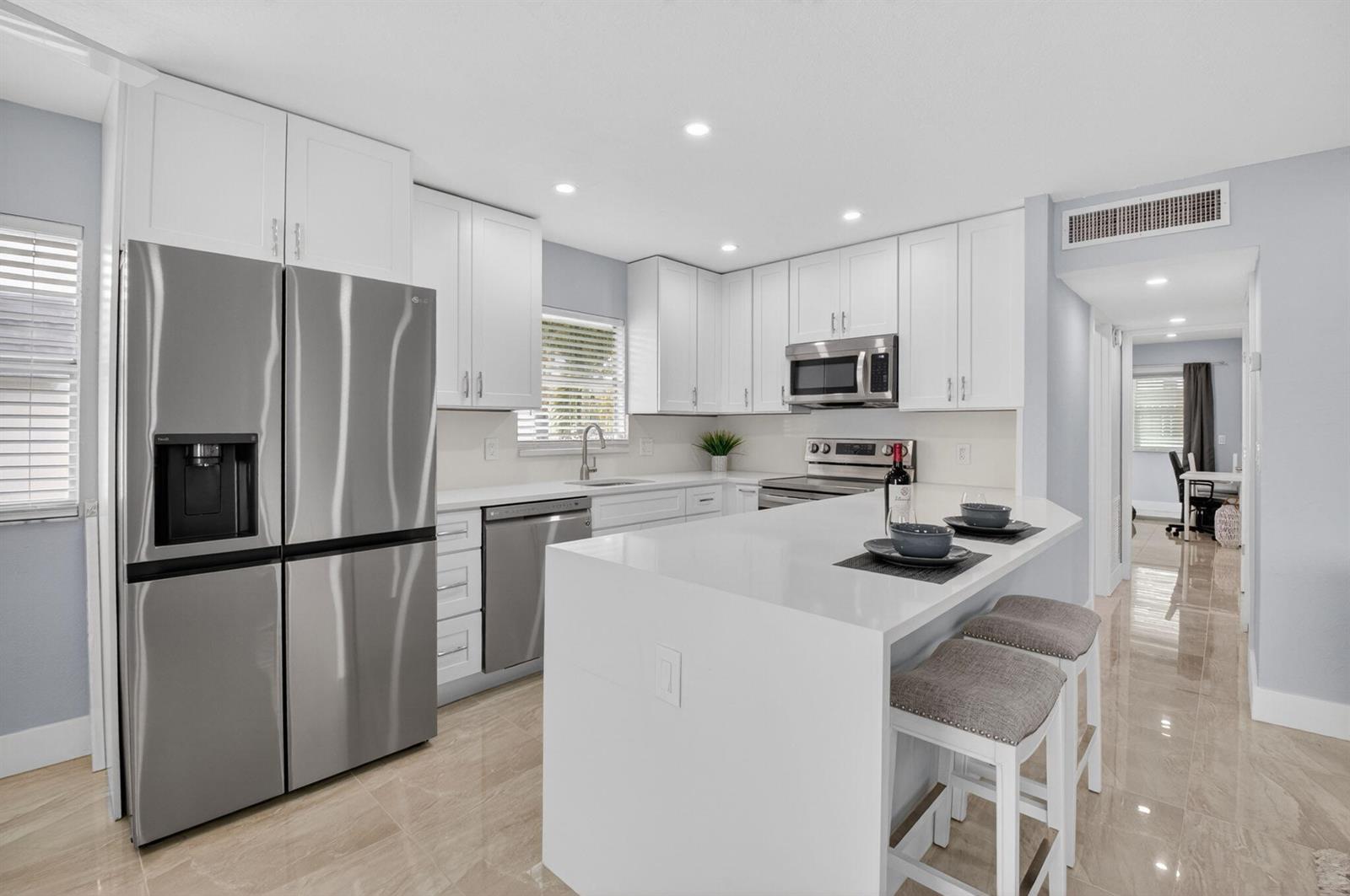 A modern kitchen features white cabinets, stainless steel appliances, and a white quartz island — 321 Saxony Trail # G, Delray Beach FL 33446, DELRAY BEACH, FL