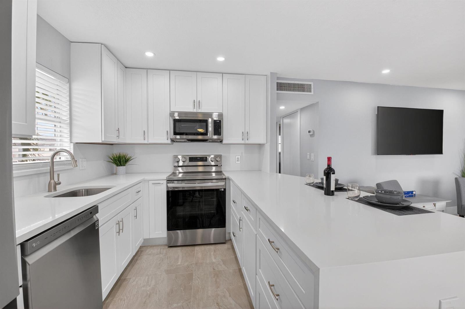 A modern kitchen features white cabinets, stainless steel appliances, and a large quartz island — 321 Saxony Trail # G, Delray Beach FL 33446, DELRAY BEACH, FL