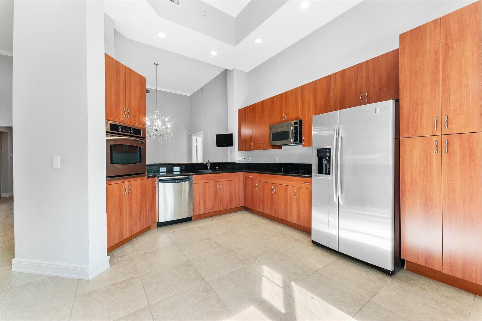 A kitchen with wood cabinets, stainless steel appliances, black countertops, and light tile flooring — 16102 Emerald Estates Drive # 101, Weston FL 33331, WESTON, FL
