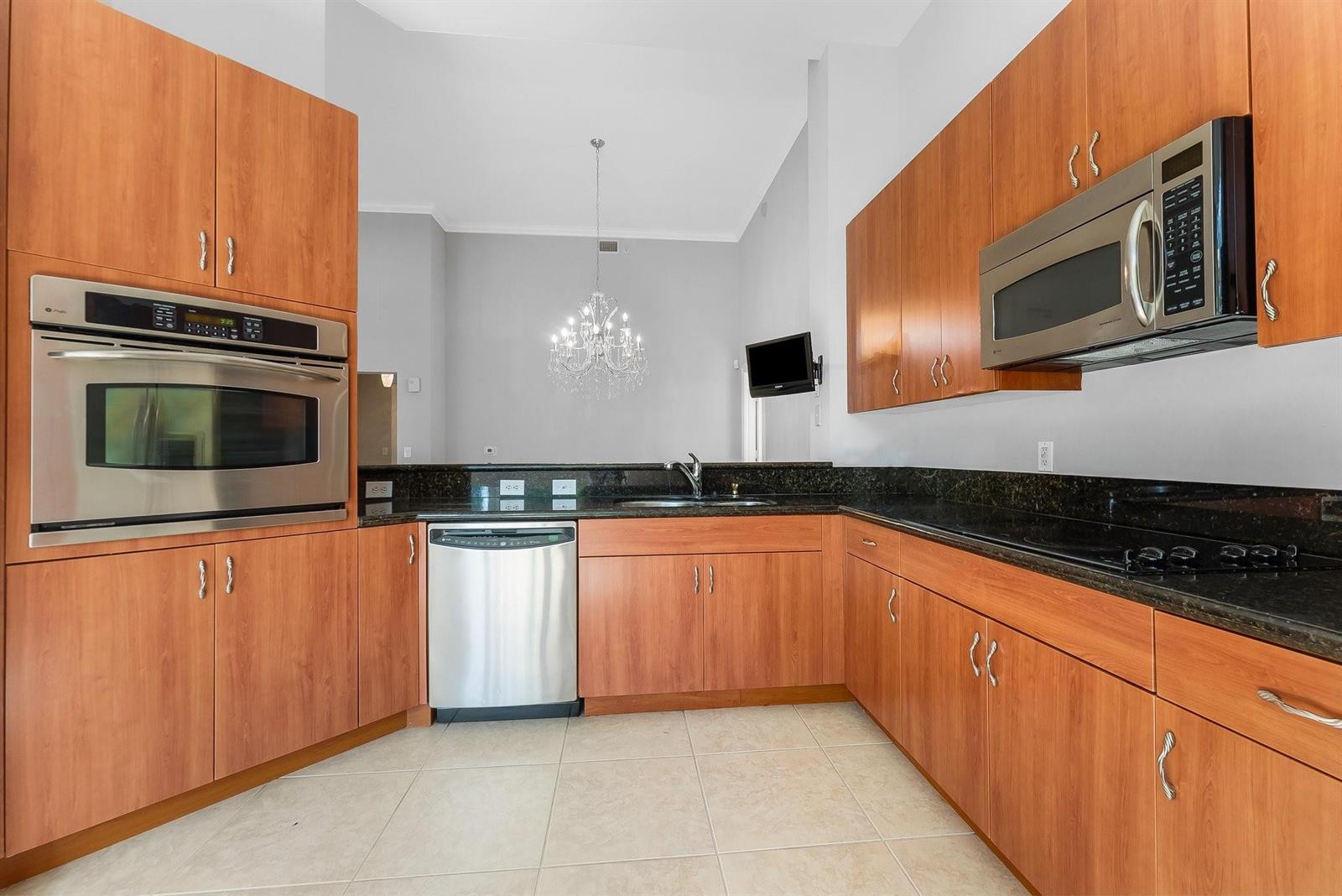 A kitchen features wood cabinets, stainless steel appliances, and dark countertops with tile flooring — 16102 Emerald Estates Drive # 101, Weston FL 33331, WESTON, FL