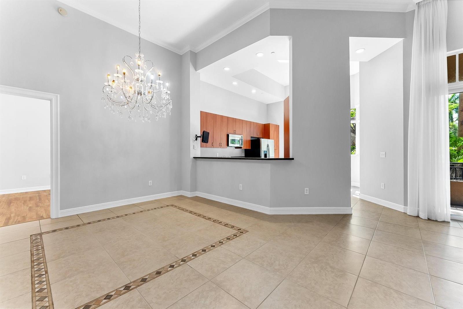 A dining area with a crystal chandelier, tiled floors, and an open kitchen pass-through — 16102 Emerald Estates Drive # 101, Weston FL 33331, WESTON, FL