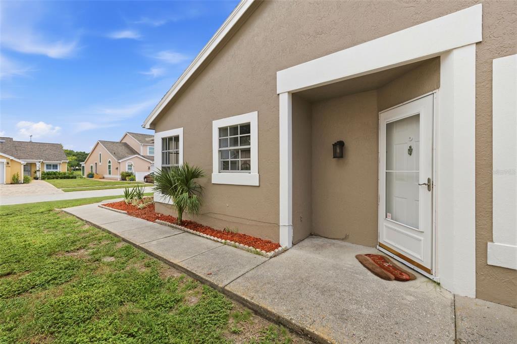 A tan stucco house exterior features a white-trimmed front door and a concrete walkway — 7705 BALHARBOUR DRIVE, NEW PORT RICHEY, FL