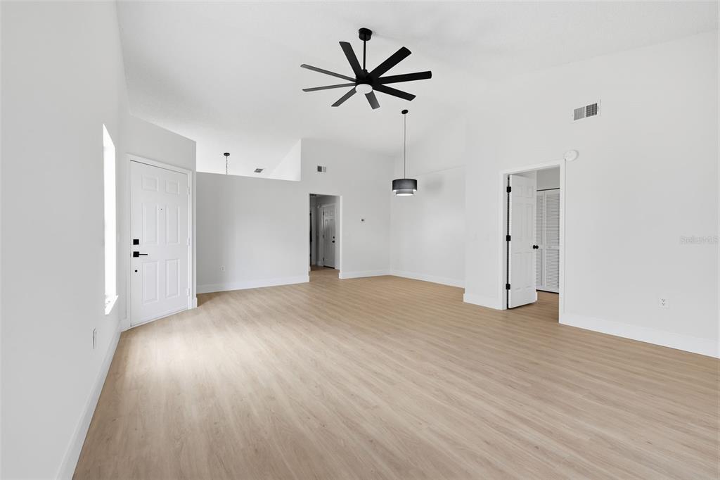 A bright, empty living area features light wood-look flooring, white walls, and a ceiling fan — 7705 BALHARBOUR DRIVE, NEW PORT RICHEY, FL