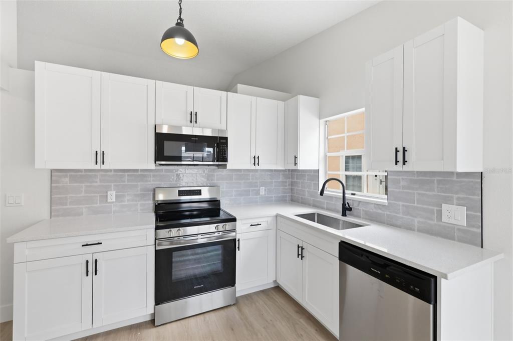 A kitchen features white cabinets, stainless steel appliances, a grey subway tile backsplash, and countertops — 7705 BALHARBOUR DRIVE, NEW PORT RICHEY, FL