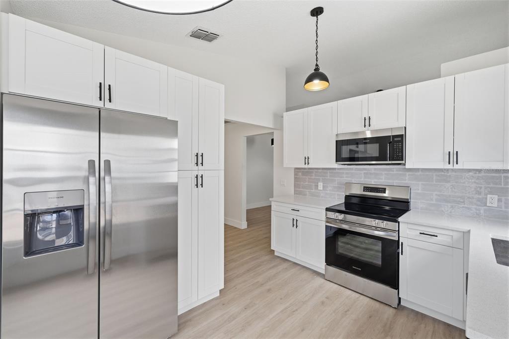 A kitchen features white cabinets, stainless steel appliances, and a gray subway tile backsplash — 7705 BALHARBOUR DRIVE, NEW PORT RICHEY, FL