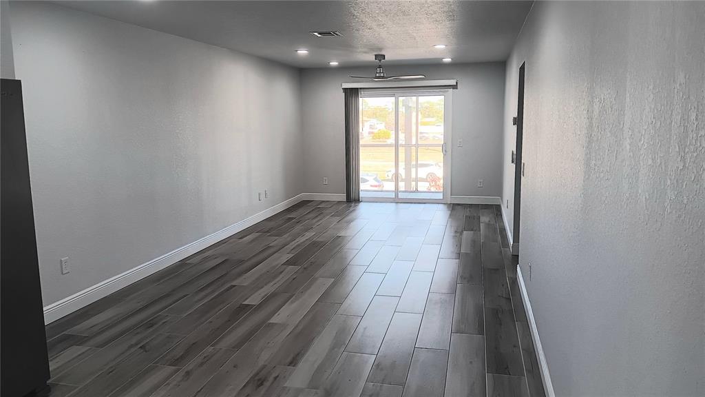 An empty room features gray walls, wood-look tile flooring, and a sliding glass door — 14506 S TAMIAMI TRAIL UNIT D, NORTH PORT, FL