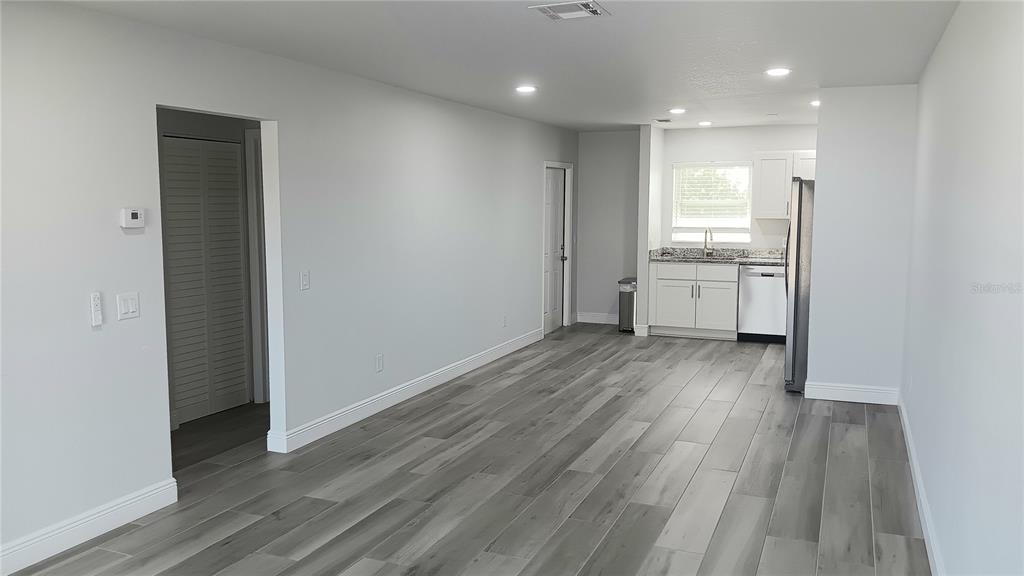 A bright, open-concept living area features gray wood-look flooring and a kitchen with white cabinets — 14506 S TAMIAMI TRAIL UNIT D, NORTH PORT, FL