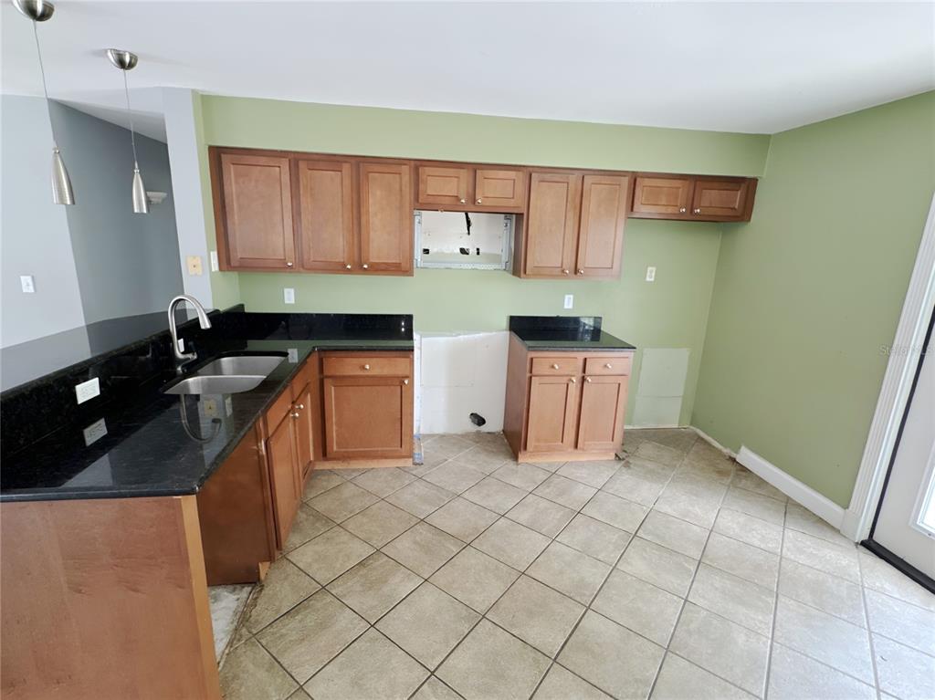 A kitchen with wood cabinets, black granite countertops, tile flooring, and light green walls — 4710 HOXIE LANE, SARASOTA, FL