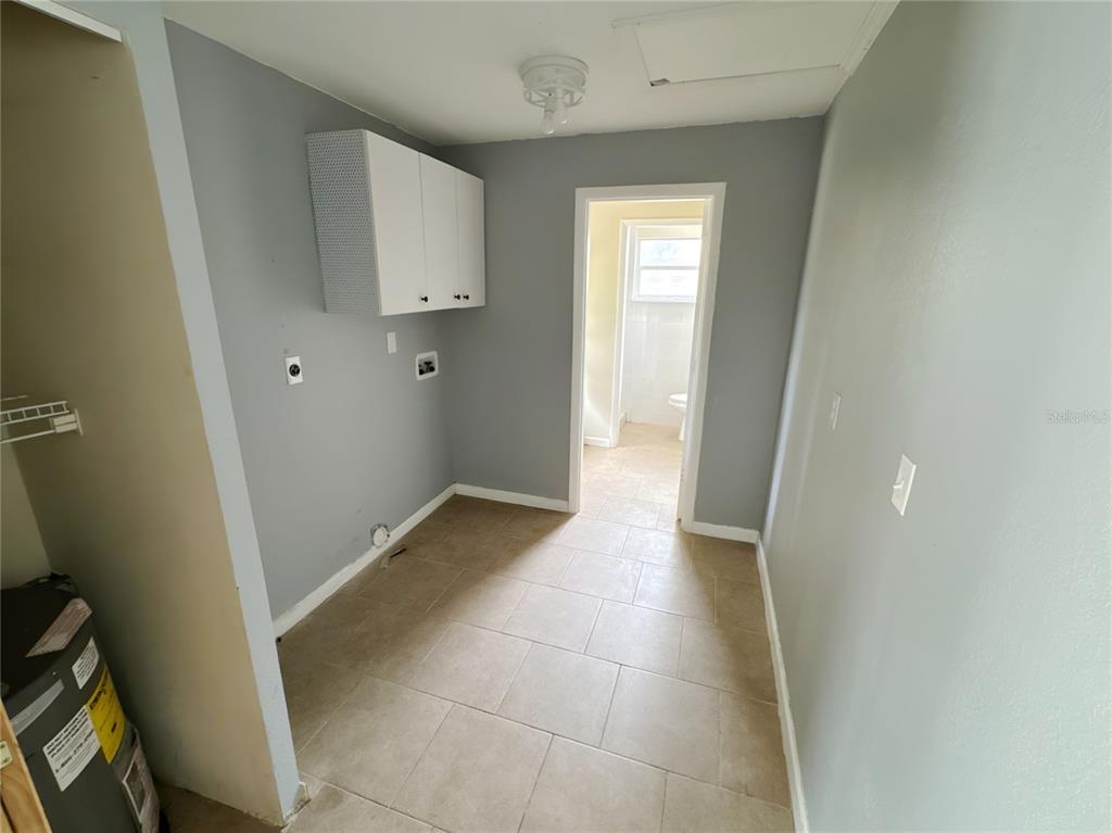 A laundry room with tile flooring, gray walls, white cabinets, and a doorway to a bathroom — 4710 HOXIE LANE, SARASOTA, FL