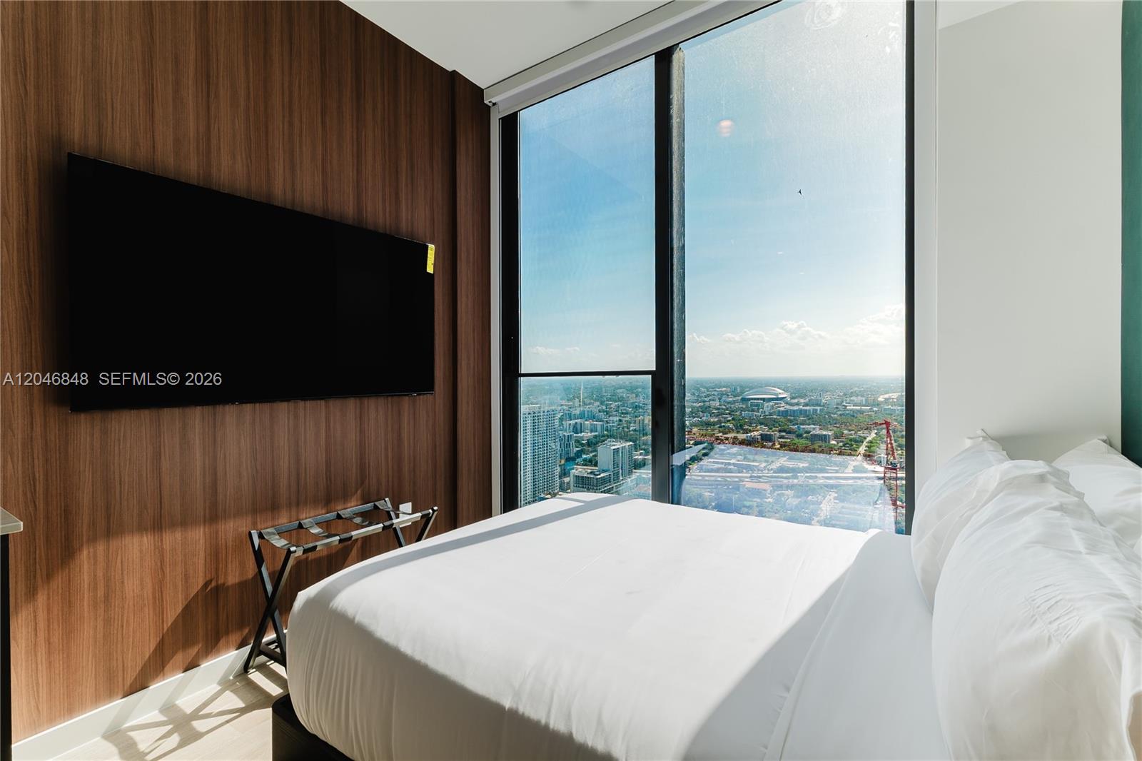 A bedroom features a wall-mounted television, wood-paneled wall, and floor-to-ceiling windows with city views — 20 NE 11th st # 4807B, Miami FL 33132, MIAMI, FL