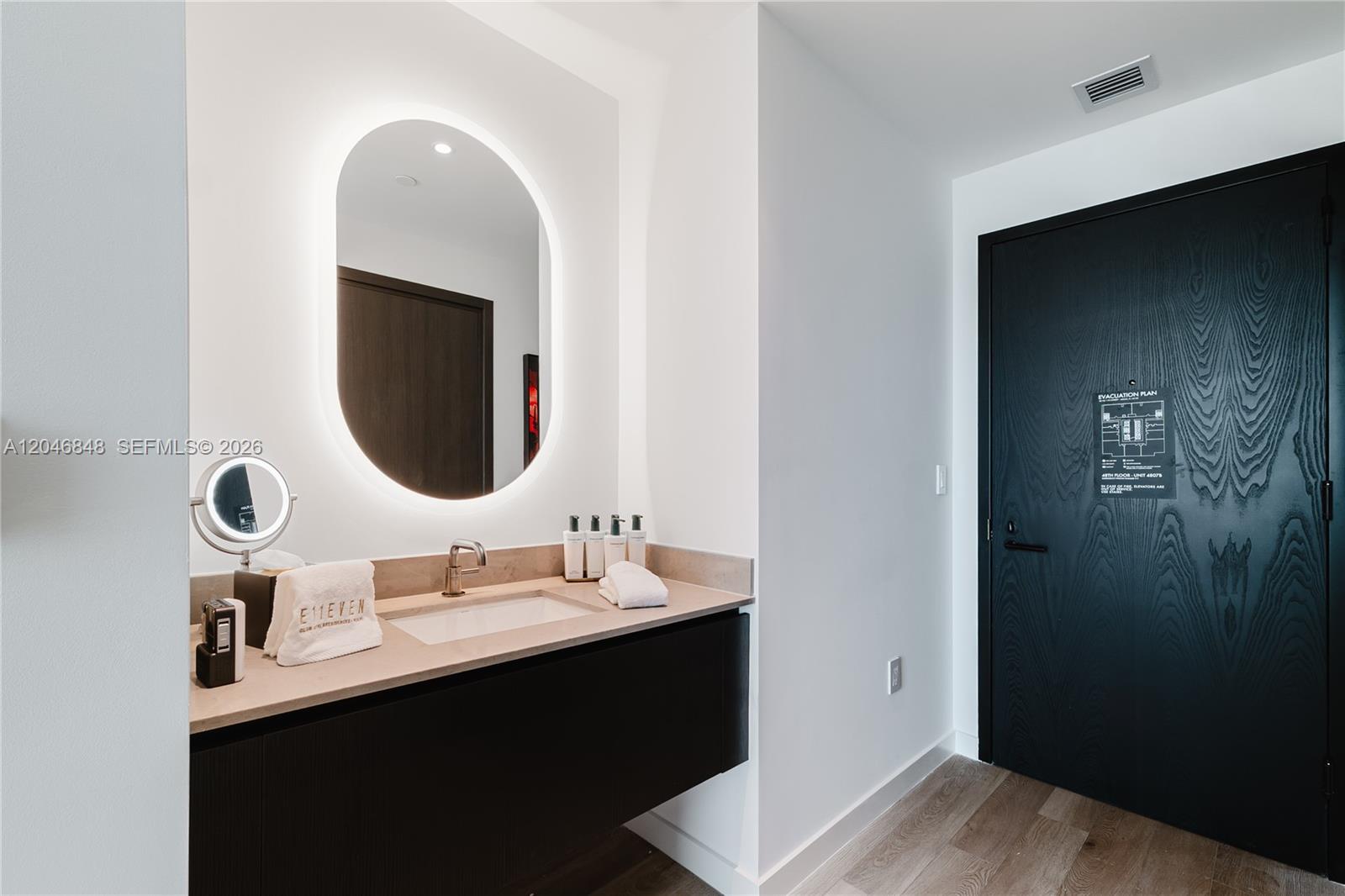 A modern bathroom features a floating vanity, an oval backlit mirror, and a black door — 20 NE 11th st # 4807B, Miami FL 33132, MIAMI, FL