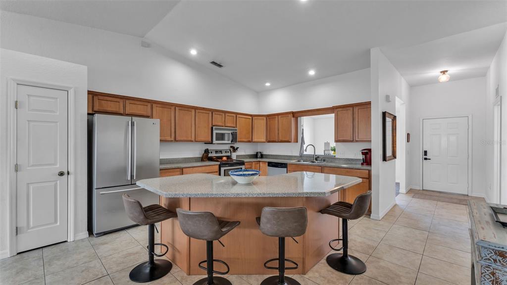 A kitchen features wood cabinets, stainless steel appliances, a granite island, and four bar stools — 6146 MISSION DRIVE, LAKELAND, FL