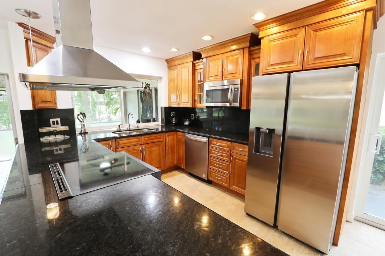 A kitchen features wood cabinets, black granite countertops, stainless steel appliances, and a range hood — 5667 Cameo Drive N, Boca Raton FL 33433, BOCA RATON, FL