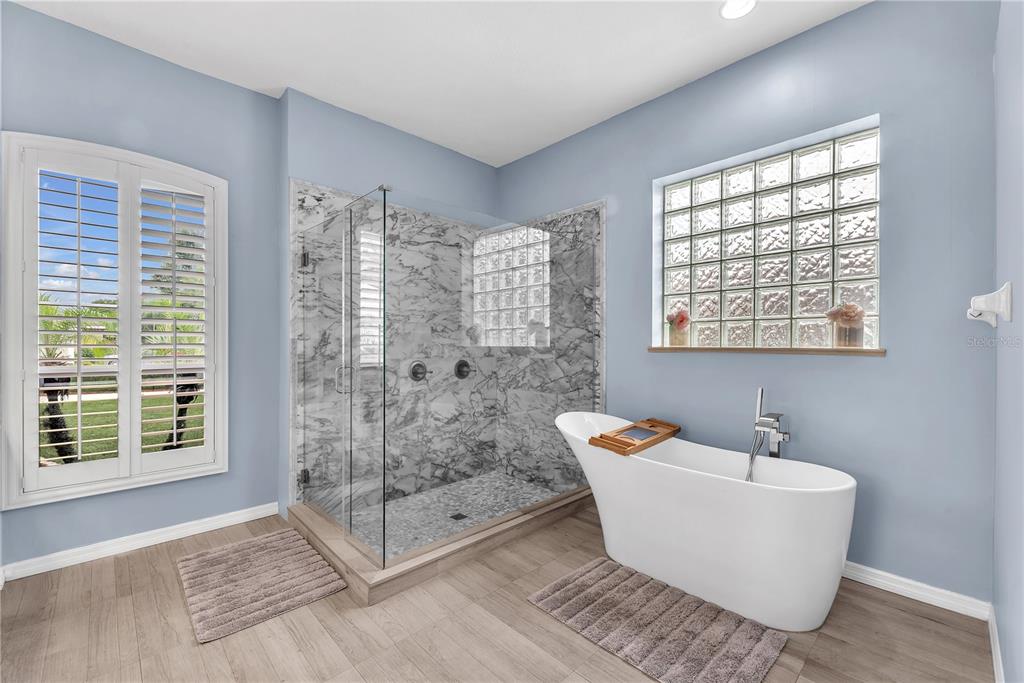 A bathroom with light blue walls, a glass-enclosed marble shower, and a white freestanding bathtub — 4419 SWIFT CIRCLE, VALRICO, FL