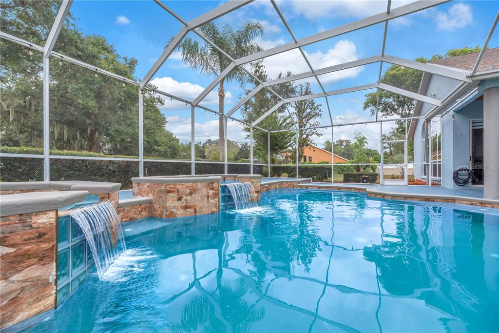 A screened-in swimming pool features stone-tiled water features and a blue patio area — 4419 SWIFT CIRCLE, VALRICO, FL