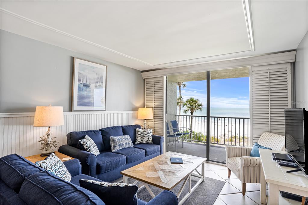 A living room with a blue sofa, coffee table, and sliding doors opening to a balcony — 20000 GULF BOULEVARD UNIT 305, INDIAN SHORES, FL