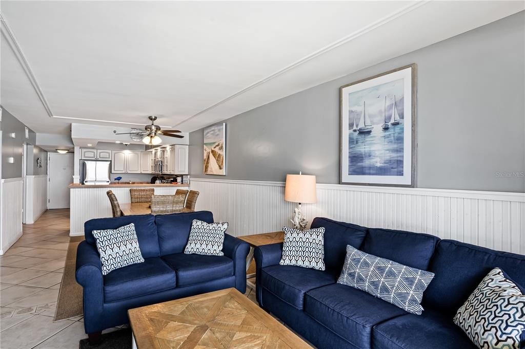 A living room features two navy blue sofas, a wooden coffee table, and white wainscoting — 20000 GULF BOULEVARD UNIT 305, INDIAN SHORES, FL