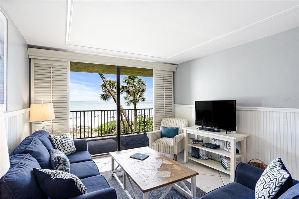 A living room features a blue sofa, a coffee table, and a balcony overlooking the ocean — 20000 GULF BOULEVARD UNIT 305, INDIAN SHORES, FL