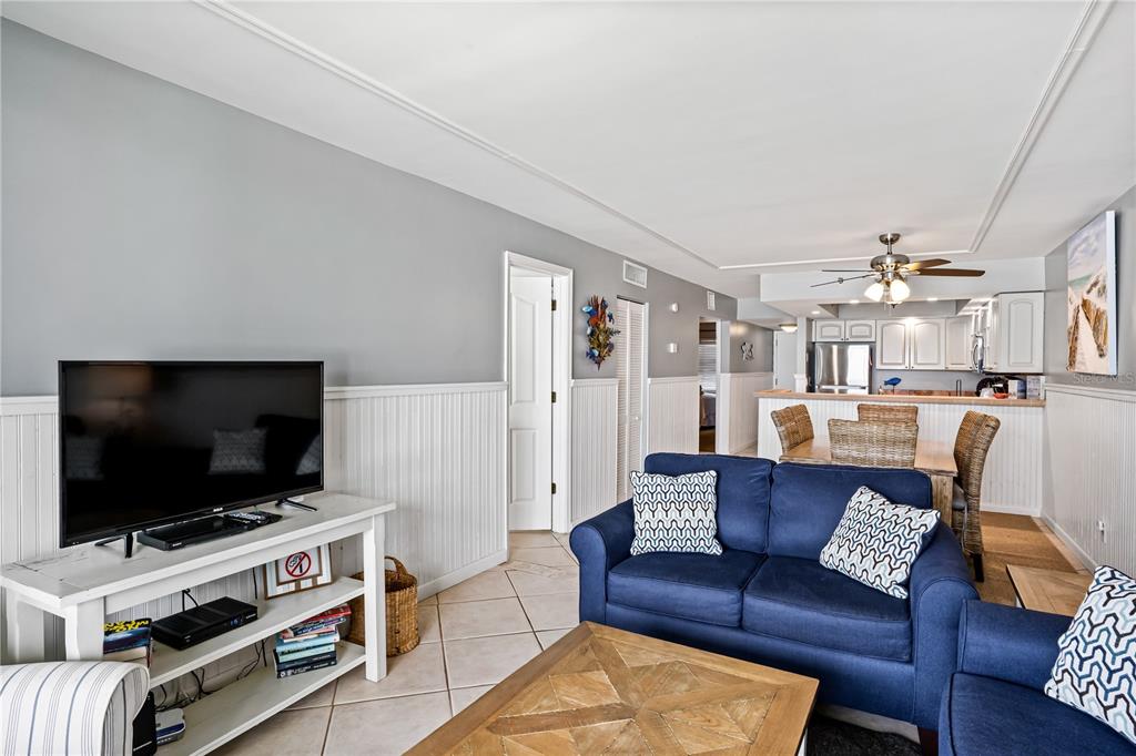 A living room with a blue sofa, white wainscoting, and an open kitchen in the background — 20000 GULF BOULEVARD UNIT 305, INDIAN SHORES, FL