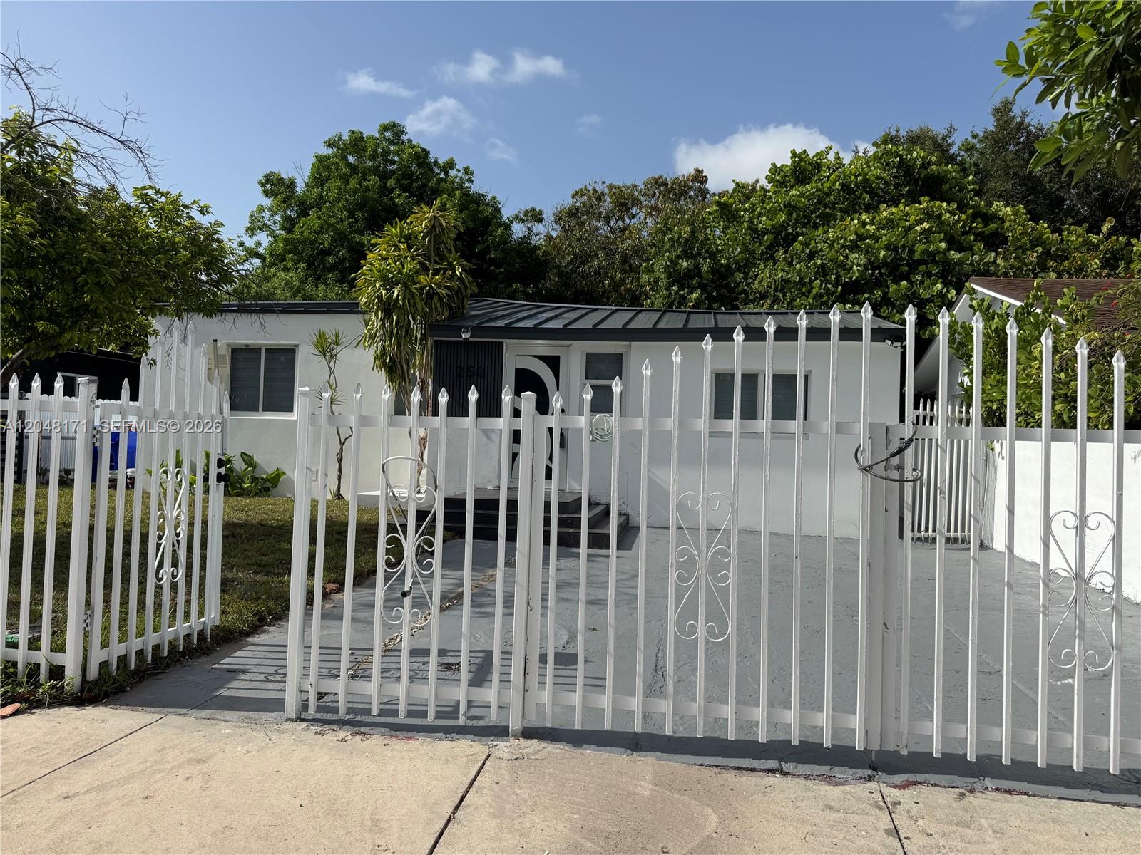 A white single-story house features a metal roof, a front porch, and a gated driveway — 250 NW 45 ST, Miami FL 33127, MIAMI, FL