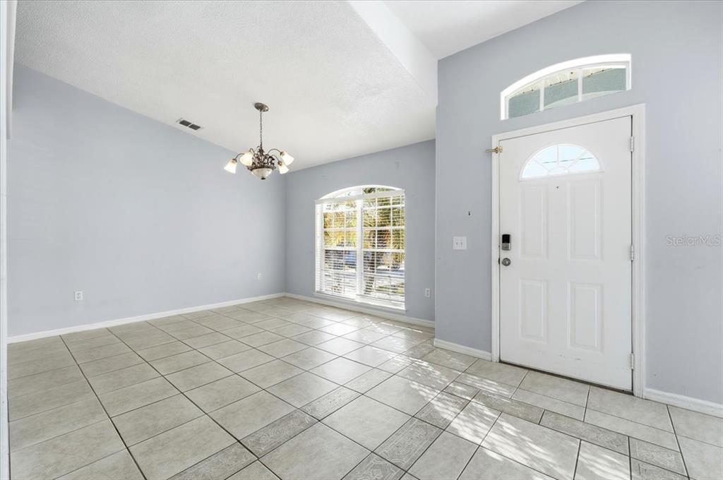 An empty room with light blue walls, tile flooring, a chandelier, and a front door — 1158 PERPIGNAN COURT, KISSIMMEE, FL