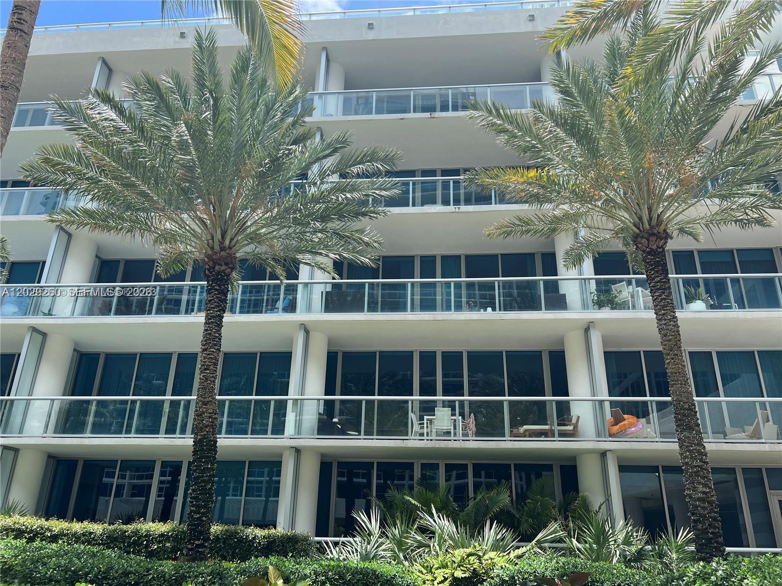 The exterior of a multi-story residential building features balconies with glass railings and palm trees — 6799 Collins Ave # 1501, Miami Beach FL 33141, MIAMI BEACH, FL