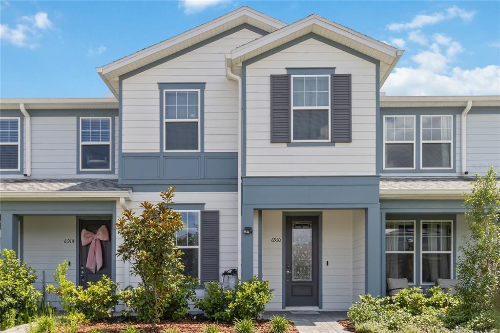 A two-story townhouse exterior features white horizontal siding, blue trim, and a covered front entrance — 6910 REVERIE PARK AVE STREET, ORLANDO, FL