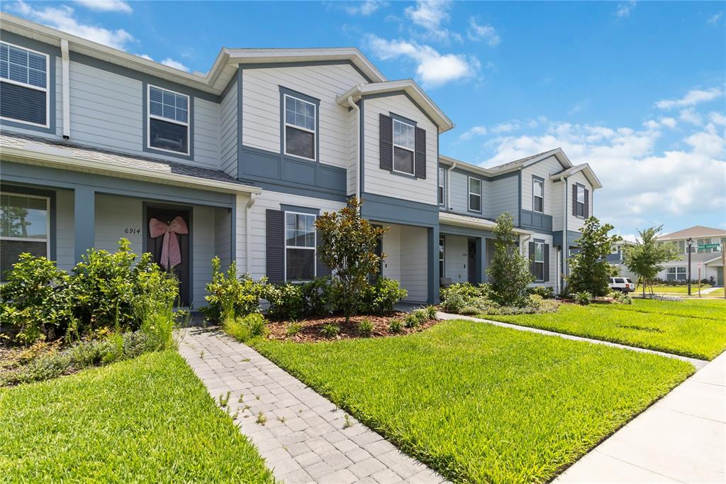 A two-story townhouse exterior features light siding, dark shutters, and a paved walkway — 6910 REVERIE PARK AVE STREET, ORLANDO, FL