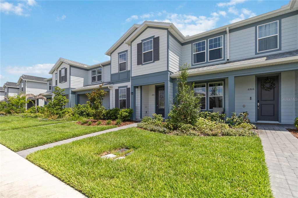 A row of two-story townhouses with light blue siding, dark trim, and landscaped front yards — 6910 REVERIE PARK AVE STREET, ORLANDO, FL