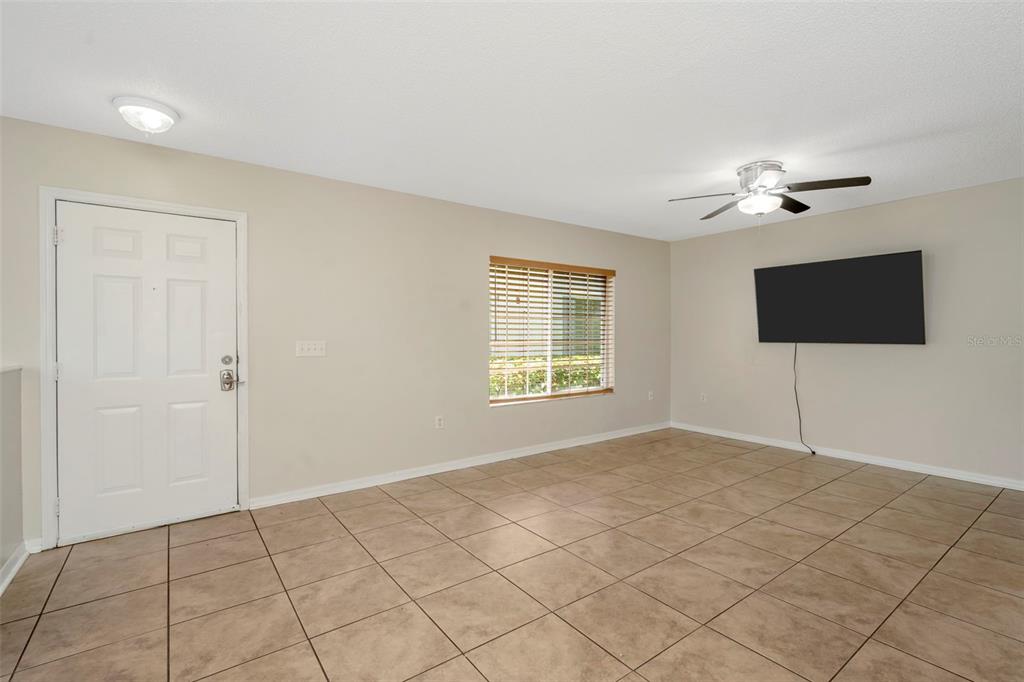A living room with beige walls, tile flooring, a ceiling fan, and a wall-mounted television — 7361 E BANK DRIVE, TAMPA, FL